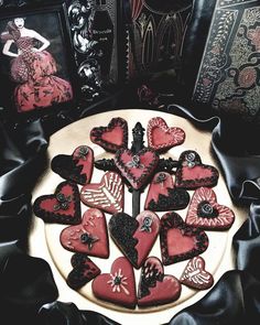 heart shaped cookies are arranged on a white plate with black satin around the edges and in front of an antique book