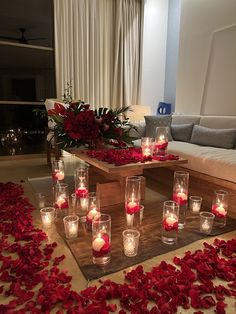 many candles are lit on the floor in front of a couch with red rose petals