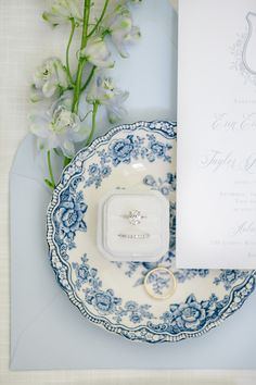 a wedding ring sits on a blue and white plate next to a bouquet of flowers