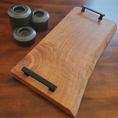 a wooden cutting board with black handles next to three rolls of toilet paper on a table