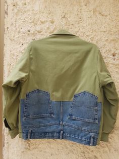 a green jacket hanging on a wall with blue jeans underneath it and the back pocket