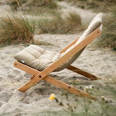 a wooden lawn chair sitting on top of a sandy beach next to grass and flowers