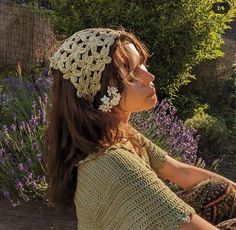 a woman wearing a crochet hat sitting on a bench in front of flowers