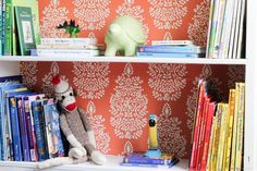 a book shelf filled with books next to a stuffed animal and wallpapered walls