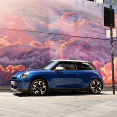 a blue mini cooper parked in front of a wall with clouds painted on it's side