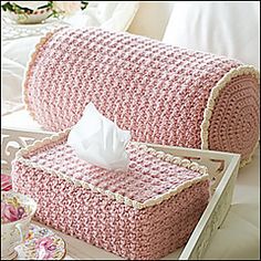 a pink crocheted box with tissue in it on a white table next to flowers