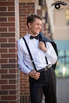 a man in a white shirt and black bow tie standing next to a brick wall