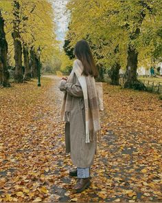 a woman is standing in the leaves looking at her cell phone while wearing a scarf