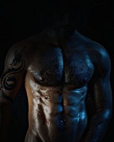 a shirtless man with tattoos on his arm and chest, standing in the dark