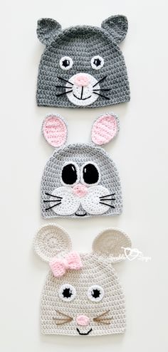 three crocheted hats with ears and eyes, one in grey the other in pink