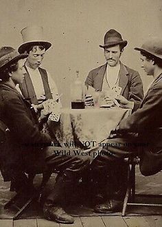 three men sitting at a table with hats on and one man holding a drink in his hand