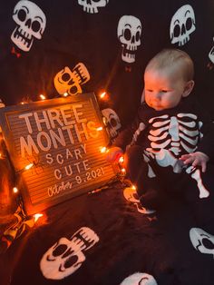 a baby sitting in front of a sign that says three month scary cute