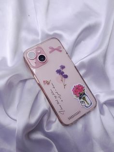 an iphone case with flowers on it laying on a white cloth covered bed sheet in the sunlight