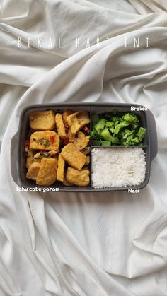 a bento box with rice, broccoli and tofu in it on a bed