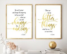 two framed art prints with gold lettering on the wall above a white table and vase