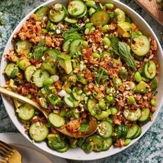 a white bowl filled with rice, cucumbers and other vegetables on top of a table