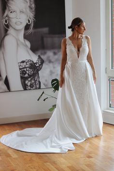 a woman standing in front of a painting wearing a wedding dress with straps and low back