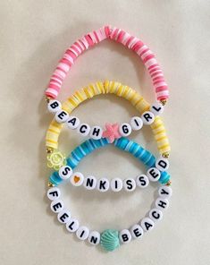 four bracelets with letters and seashells are arranged on a white table top