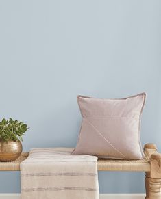 a wooden bench with a pillow on top of it next to a potted plant