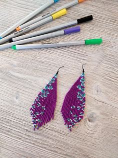 the beaded earrings are next to markers and pencils on a wooden table with colored crayons