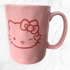 a pink hello kitty coffee mug with a red bow on it's head and eyes