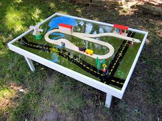 a child's table with a toy train set on it in the middle of grass