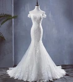 a white wedding dress on a mannequin in front of a blue wall and potted plant