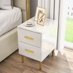 a white nightstand with gold handles next to a bed