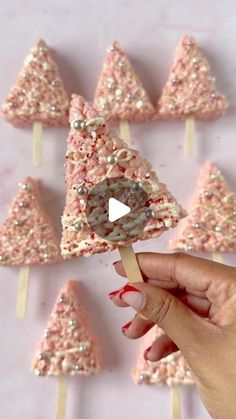 a person holding a lollipop in front of some pink and silver trees on sticks