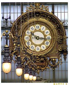 an ornate clock hanging from the side of a building with chandeliers around it