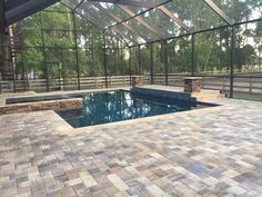 an outdoor pool surrounded by glass walls and brick pavers flooring is shown in the foreground