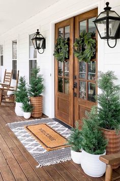 the front porch is decorated with potted plants and wreaths on the door mat