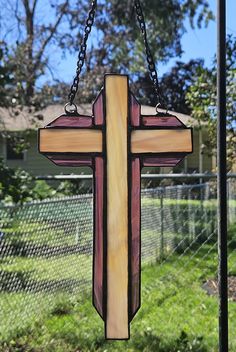 a stained glass cross hanging from a chain in front of a fenced in yard