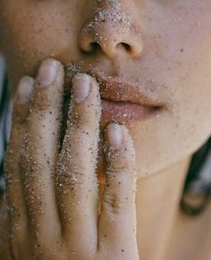 a close up of a person holding their hand to her face with sand all over them