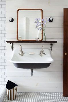 a white sink sitting under a bathroom mirror next to a wooden shelf filled with flowers