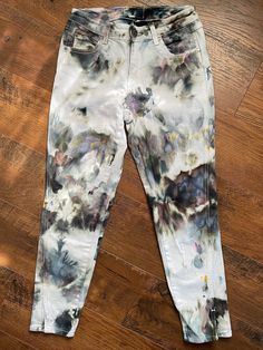 a pair of white jeans with black and blue paint splattered on them sitting on top of a wooden floor