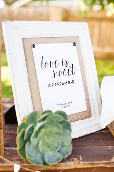 an ice cream bar sign sitting on top of a wooden table next to a succulent