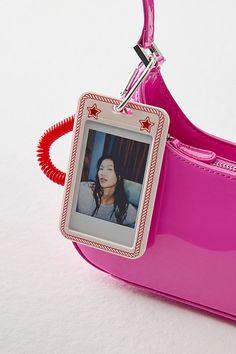 a pink purse with a photo hanging from it's front loop and a red cord attached to the handle