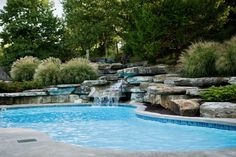 an outdoor swimming pool surrounded by rocks and water features a waterfall that runs down the side of it