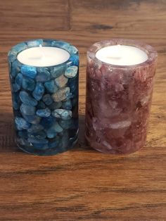 two candles sitting on top of a wooden table next to each other with rocks in them