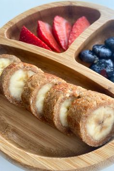 a wooden plate topped with sliced bananas next to blueberries and strawberries on top of it