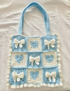 a crocheted blue and white purse with bows on the handles is laying on a bed