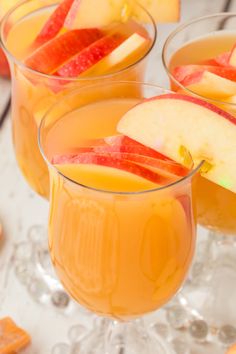 three glasses filled with apple cider and garnished with sliced apples on the side