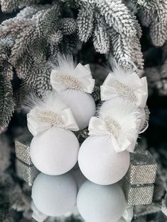 three white balls with bows on them are sitting in front of some pine cones and fir branches