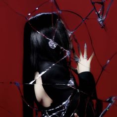 a woman with black hair and nails standing in front of a red wall holding her hands up