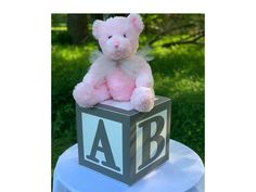 a pink teddy bear sitting on top of a block with the letters a and b