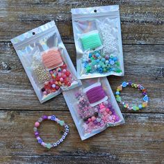 three bags filled with different types of beads and hair accessories sitting on top of a wooden table