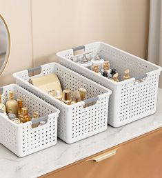 three white baskets with gold and silver items in them on a counter top next to a mirror