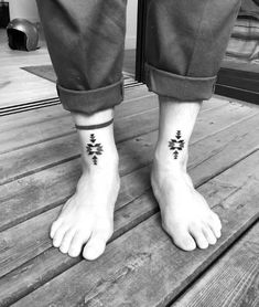 two people with tattoos on their feet standing on a wooden platform in front of a door