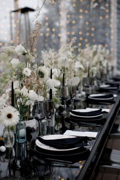 a long table is set with black and white plates, silverware, and flowers